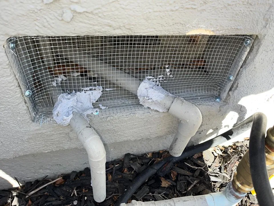 Vent covered with screwed-in steel mesh, the two pipes through it sealed with putty