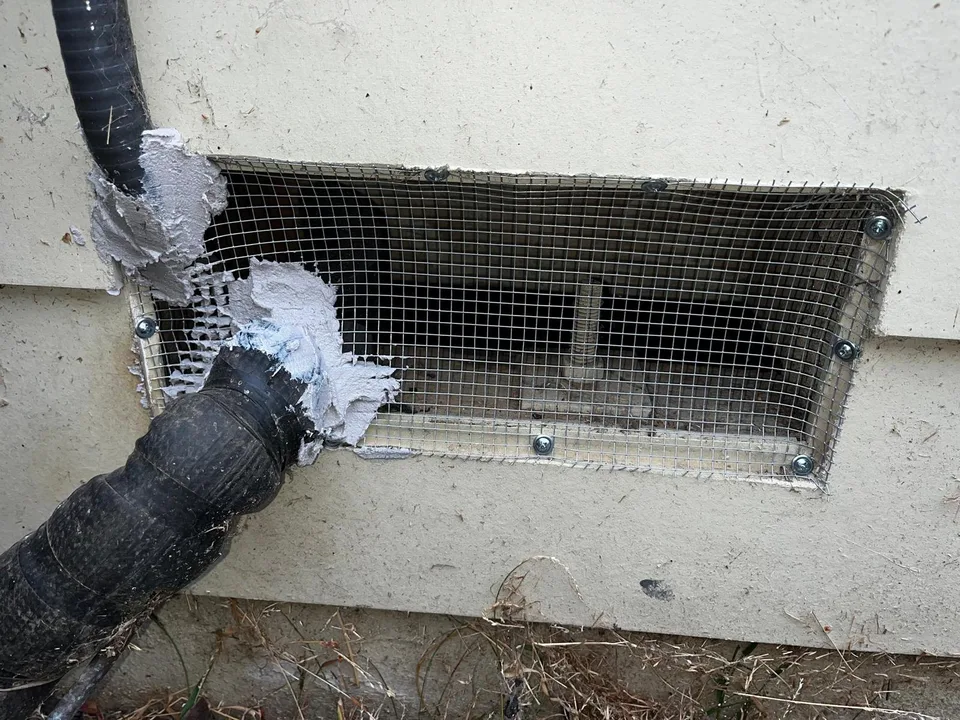 Pipe gaps around a crawl space vent sealed with putty over galvanized steel mesh