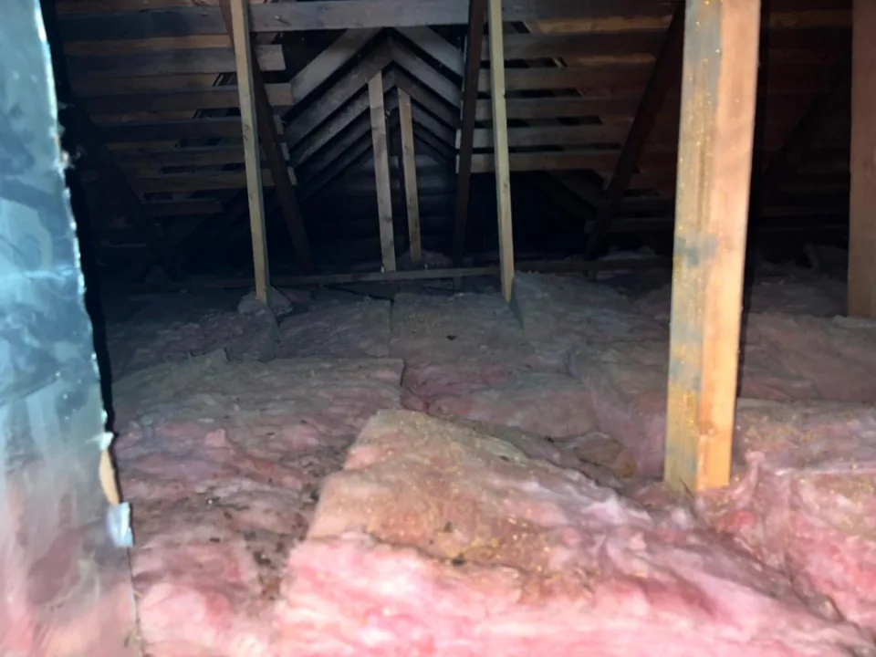 Closer view of the same attic before the job: old pink batts, dusty and uneven, between wooden posts